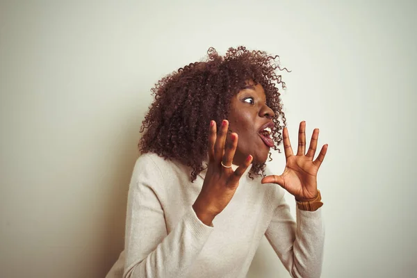 Young african afro woman wearing turtleneck sweater over isolated white background crazy and mad shouting and yelling with aggressive expression and arms raised. Frustration concept.