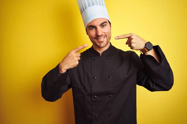 制服を着た若い料理人が 黄色い背景の上に立ち 明るい表情と指や口で指差す 歯科衛生の概念 — ストック写真