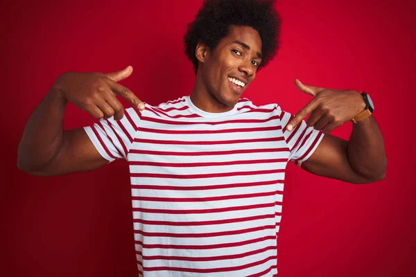 年轻的非洲裔美国人 留着黑发 穿着条纹T恤 披着孤零零的红色背景 面带微笑 带着自信 用手指指着自己 自豪而快乐 — 图库照片