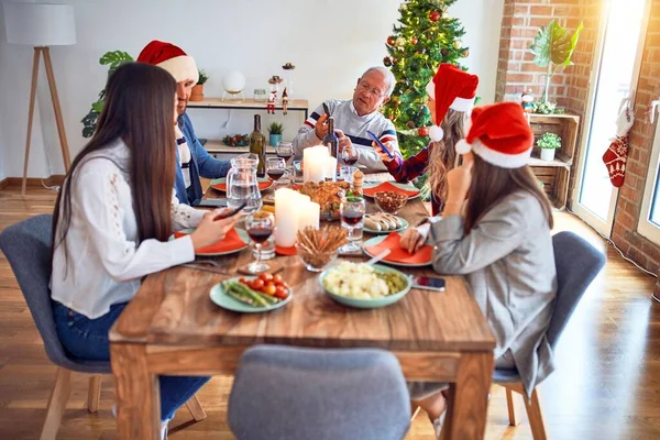 美丽的家庭戴着圣诞礼帽 面带微笑 快乐而自信 在家里用智能手机吃烤火鸡庆祝圣诞节 — 图库照片
