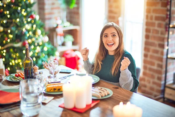 自宅でクリスマスツリーの周りに食べ物を食べて座っている若い美しい女性は 腕を上げて目を開けて成功したことに驚きと驚きを祝います 勝者のコンセプト — ストック写真