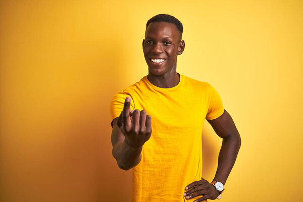 Young african american man wearing casual t-shirt standing over isolated yellow background Beckoning come here gesture with hand inviting welcoming happy and smiling