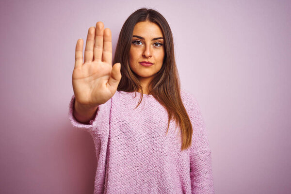 Young beautiful woman wearing casual sweater standing over isolated pink background doing stop sing with palm of the hand. Warning expression with negative and serious gesture on the face.