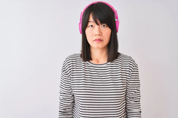 中国妇女在孤立的白色背景下 用粉色耳机听音乐 脸上表情严肃 简单而自然地看着相机 — 图库照片