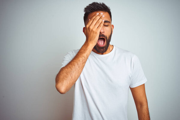 Young indian man wearing t-shirt standing over isolated white background Yawning tired covering half face, eye and mouth with hand. Face hurts in pain.