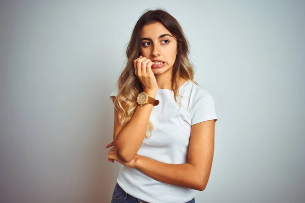 Young beautiful woman wearing casual white t-shirt over isolated background looking stressed and nervous with hands on mouth biting nails. Anxiety problem.