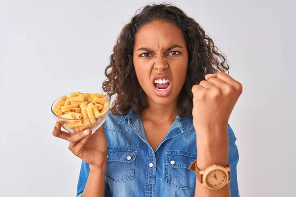 若いですブラジル人女性保持ボウルでマカロニパスタ上の隔離された白い背景いらいらとフラストレーション怒りと叫びます クレイジーと大声で上げ手 怒りの概念 — ストック写真