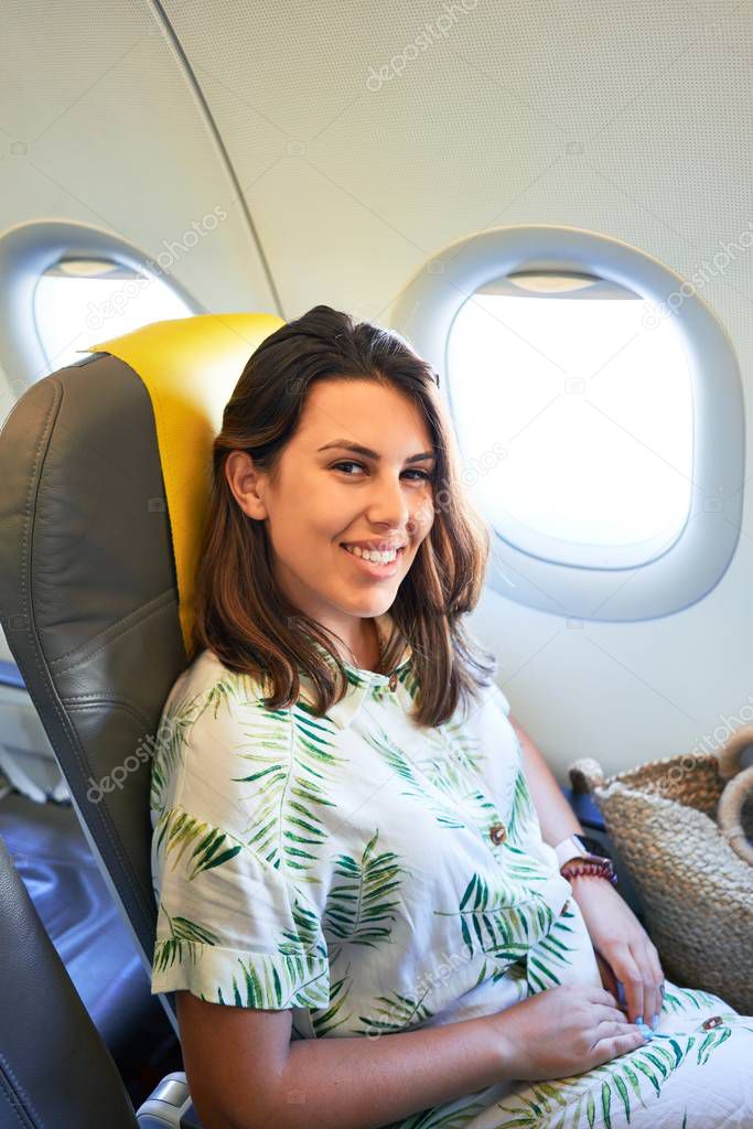 Young traveller woman sitting inside plane at the airport with sky view from the window
