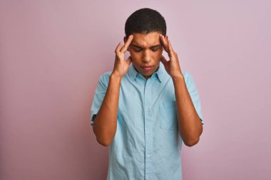 Genç, yakışıklı, mavi gömlekli bir Arap, pembe arka planda duruyor. Başında baş ağrısı var çünkü stres var. Migren ağrısı..