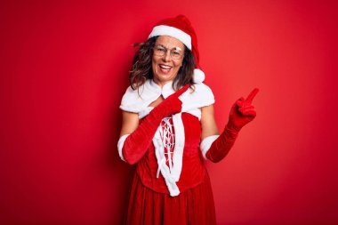 Orta yaşlı güzel bir kadın Noel Baba kostümü giyiyor. Kırmızı arka planda. Gülümsüyor ve kameraya bakıyor..