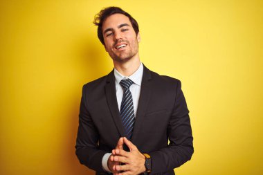 Sarı arka plan üzerinde duran takım elbiseli ve kravatlı genç yakışıklı işadamı ellerini birleştirip gülümseyerek gevşemiş ve neşeli olmasını diliyordu. Başarı ve iyimser