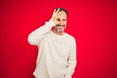 Yakışıklı orta yaşlı, gri saçlı, izole edilmiş kırmızı arka planda son sınıf öğrencisi. El hareketleriyle gülümsüyor, gözleriyle mutlu yüzüyle parmaklarının arasından bakıyor..