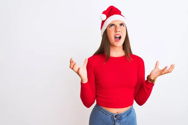 年轻美丽的女孩戴着圣诞圣诞圣诞礼帽 站在孤独的白色背景上 疯狂地大叫着 带着咄咄逼人的表情和手臂大喊大叫 沮丧的概念 — 图库照片