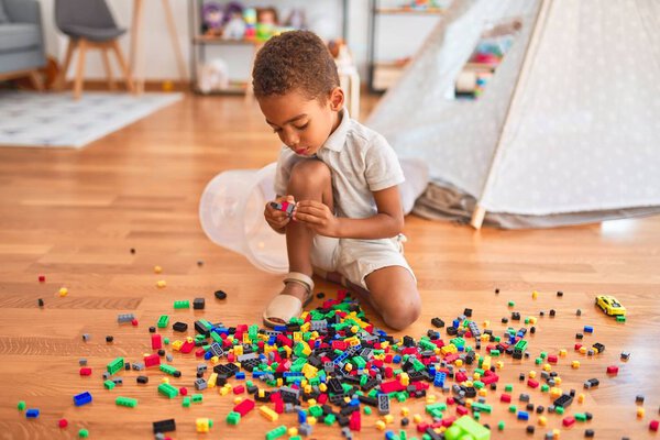 Beautiful african american toddler playing with small building blocks at kindergarten