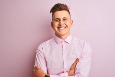 Soyutlanmış pembe arka plan üzerinde duran şık gömlekli genç yakışıklı işadamı kameraya bakarken kollarını çaprazlayarak gülümsüyor. Pozitif kişi.