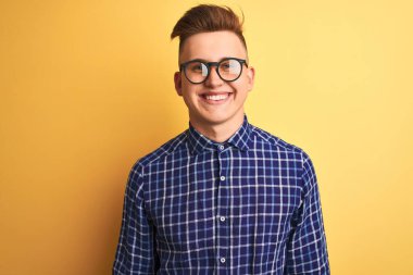 Yüzünde mutlu ve havalı bir gülümseme olan, izole edilmiş sarı arka plan üzerinde gündelik gömlek ve gözlük takan genç yakışıklı bir adam. Şanslı kişi..