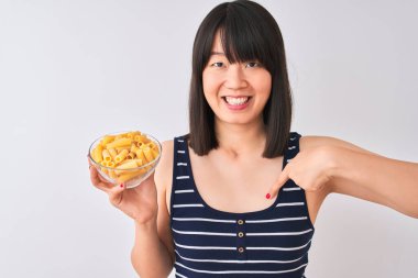 Genç, güzel bir Çinli kadın makarna kasesini izole edilmiş beyaz arka planda tutuyor. Sürpriz yüz ifadesi kendini gösteriyor.