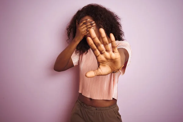孤立したピンクの背景の上にTシャツを着た若いアフリカ系アメリカ人女性が手で目を覆い 悲しいと恐怖の表情でジェスチャーを止めます 恥ずかしいと否定的な概念 — ストック写真
