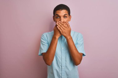 Mavi gömlekli genç, yakışıklı bir Arap, pembe arka planda dikiliyor. Ağzını yanlışlıkla ellerle kapatıyor. Gizli konsept.