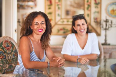 Güzel anne ve kızı evde oturup konuşuyor ve gülümsüyor.