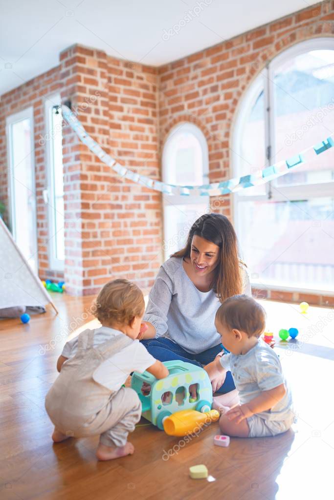 Beautiful teacher and toddlers playing around lots of toys at kindergarten