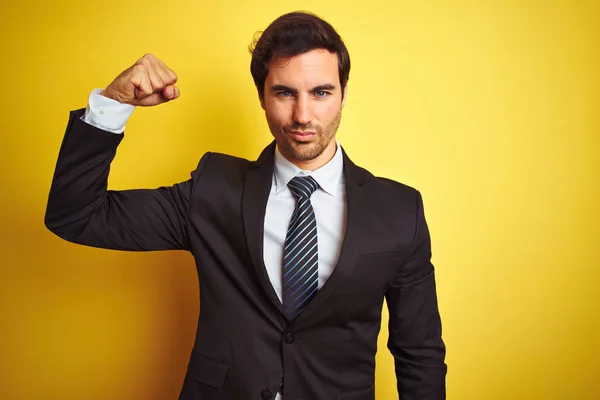 若いハンサムなビジネスマンがスーツを着て 孤立した黄色の背景の上に立ってネクタイ腕の筋肉を示す強い人 自信と力の誇り — ストック写真