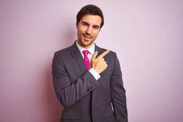 若いハンサムなビジネスマンがスーツを着て 顔を指して笑顔で陽気に孤立したピンクの背景の上に立ってネクタイ手と指で顔に幸せと自然な表情で側面まで — ストック写真