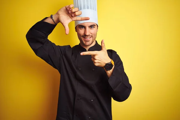 制服を着た若い料理人が 黄色い背景の上に立ち 手と指で幸せそうな顔をしたフレームを作っている 創造性と写真の概念 — ストック写真