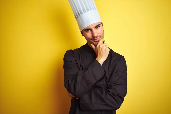 年轻厨师 身穿制服 头戴帽子 站在孤立的黄色背景上 看着相机 自信地微笑着 双臂交叉 双手托着下巴 积极地思考 — 图库照片