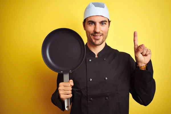 年轻的厨师 身穿制服 头戴帽子 把锅盖在孤立的黄色背景上 惊讶地发现有一个想法或问题 他满脸喜形于色 指手画脚 位居第一 — 图库照片