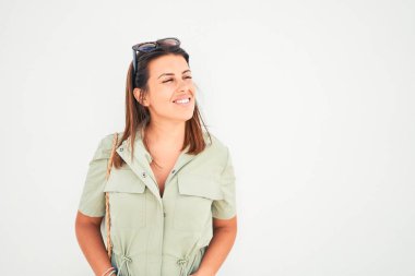 Güzel kız beyaz duvara yaslanıyor, genç arkadaş canlısı kadın mutlu bir yaz gününde gülümsüyor.