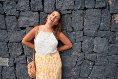 Güzel kız duvara yaslanıyor, genç arkadaş canlısı kadın mutlu bir yaz gününde gülümsüyor.