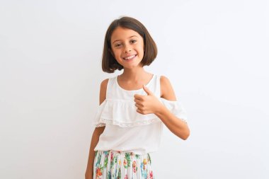 İzole edilmiş beyaz arka planda dikilen gündelik elbiseler giyen genç ve güzel bir kız çocuğu mutlu bir el hareketi yapıyor. Kameraya bakıp başarıyı gösteren ifade onaylanıyor.