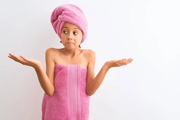漂亮的小女孩洗完澡后穿着浴巾 站在孤独的白色背景上 毫无头绪 满脸困惑地举起胳膊和双手 怀疑的概念 — 图库照片