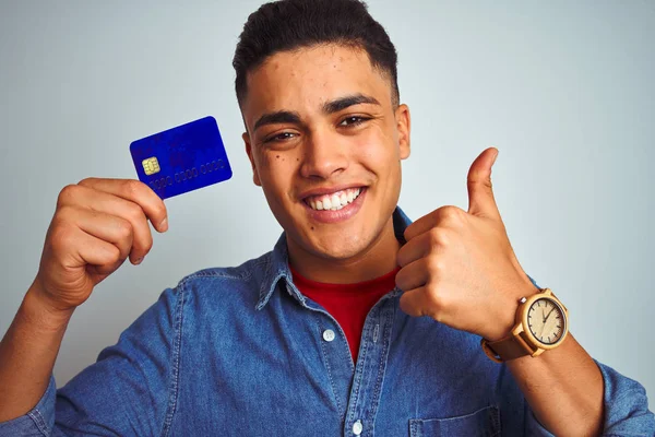 年轻的巴西顾客持信用卡站在孤立的白色背景上 开心的笑着做个好手势 用手指竖起大拇指 出色的标志 — 图库照片