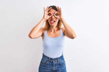 Güzel kızıl saçlı kadın izole edilmiş arka planda duruyor. Dürbün gibi jest yapıyor. Dürbün dilini çıkarıyor, gözler parmaklarından bakıyor. Çılgın ifade.