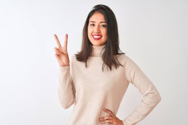 Balıkçı yaka kazak giyen güzel Çinli kadın izole edilmiş beyaz arka planda durup parmaklarını zafer işareti yaparken gösteren kameraya gülümsüyor. İki numara..