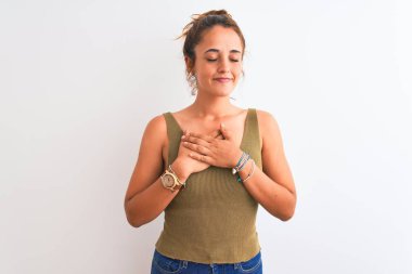 Genç kızıl saçlı bir kadın izole edilmiş arka planda topuz takıyor. Elleri göğsünde, gözleri kapalı ve yüzünde minnet dolu bir jest ile gülümsüyor. Sağlık kavramı.