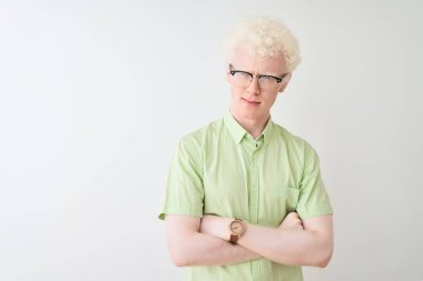 Yeşil tişörtlü ve gözlüklü genç sarışın adam izole edilmiş beyaz arka plan şüphecisi ve gergin, yüzünde çapraz kollu tasvip etmeyen bir ifade var. Negatif kişi.