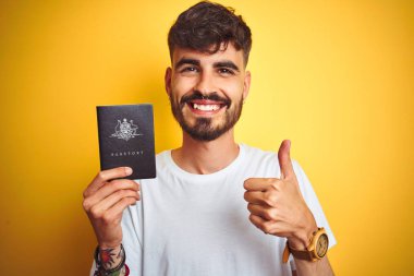 Avustralya pasaportlu, dövmeli genç adam izole edilmiş sarı arka planda mutlu, gülümseyen, işaret veren, parmaklarıyla baş parmağı olan, mükemmel bir işaret.