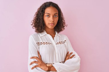 Genç Brezilyalı kadın giyen gömlek ayakta üzerinde izole pembe arka plan yüzünde ciddi bir ifade ile rahat. Çapraz kollar ile basit ve doğal