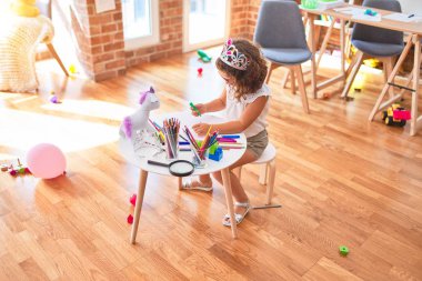 Güzel bebek gözlük takıyor ve prenses tacı takıyor. Anaokulunda kağıt ve keçeli kalemle çiziyor.