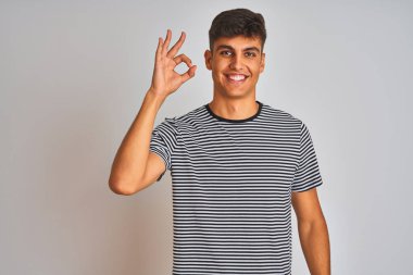 İzole edilmiş beyaz arka planda duran, donanma çizgili tişört giyen genç Hintli adam el ve parmaklarıyla 