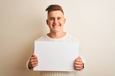 İzole edilmiş beyaz arka planda elinde pankart tutan genç yakışıklı bir adam mutlu bir yüzü olan ve kendine güvenen bir gülümsemeyle dişlerini gösteren.