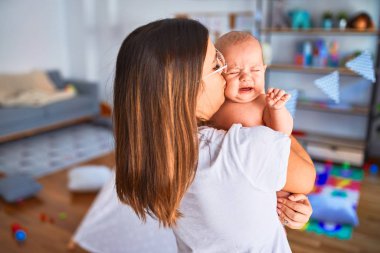 Genç, güzel bir kadın ve bebeği evde duruyor. Anne kucağında ve yeni doğan bebeği öpüyor.