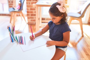 Anaokulunda renkli kalemler kullanarak güzel bir kız güzel çizim yapıyor.