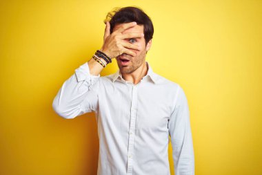 Zarif bir iş adamı şık bir gömlek giyer, izole edilmiş sarı arka planda dikilir. Şoka girer, yüzünü ve gözlerini kapar, utanmış bir ifadeyle parmaklarının arasından bakar..