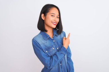 İzole edilmiş beyaz arka planda dikilen kot gömlek giyen genç, güzel Çinli bir kadın. Yüzünde mutlu ve doğal bir ifadeyle, elleri ve parmaklarıyla yüzünü gösteren bir gülümseme.