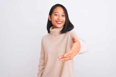 Balıkçı yaka kazak giyen genç Çinli kadın izole edilmiş beyaz arka planda durup dostça gülümseyerek selamlama ve hoş geldin diyor. Başarılı bir iş..