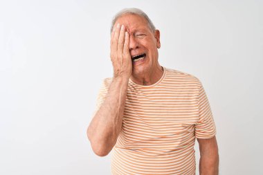 İzole edilmiş beyaz arka planda duran çizgili tişört giyen yaşlı, gri saçlı adam esnemekten yorgun düşmüş, yüzünü, gözünü ve ağzını eliyle kapatıyor. Yüzüm acıyor..